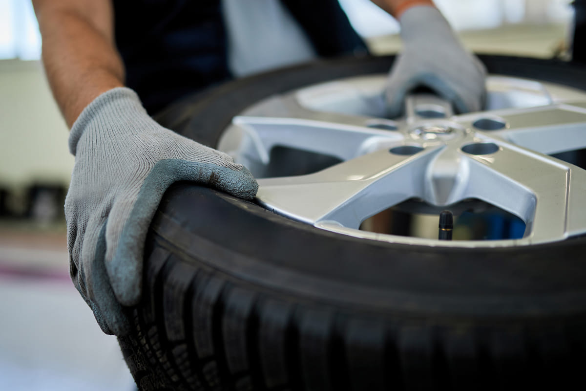 Mechanic wearing grey gloves handling car tire