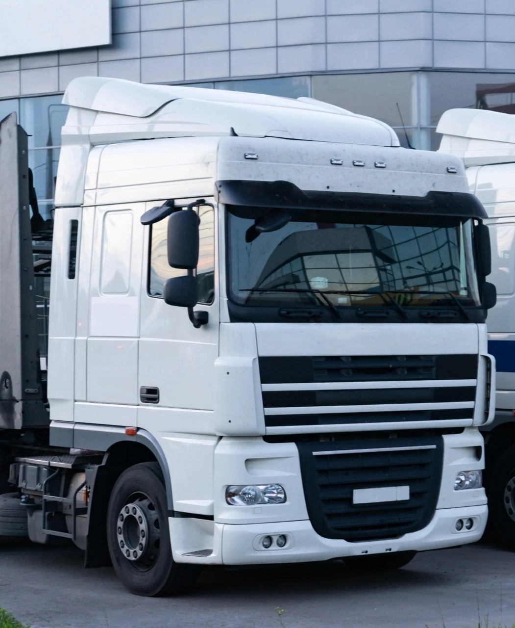 White commercial truck parked neck to another commercial vehicle