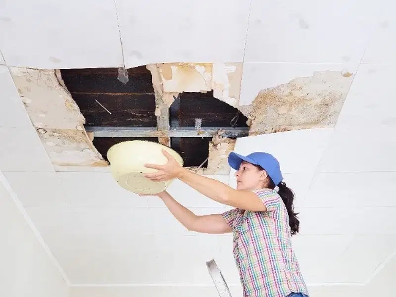 Woman catching ceiling leak in bucket