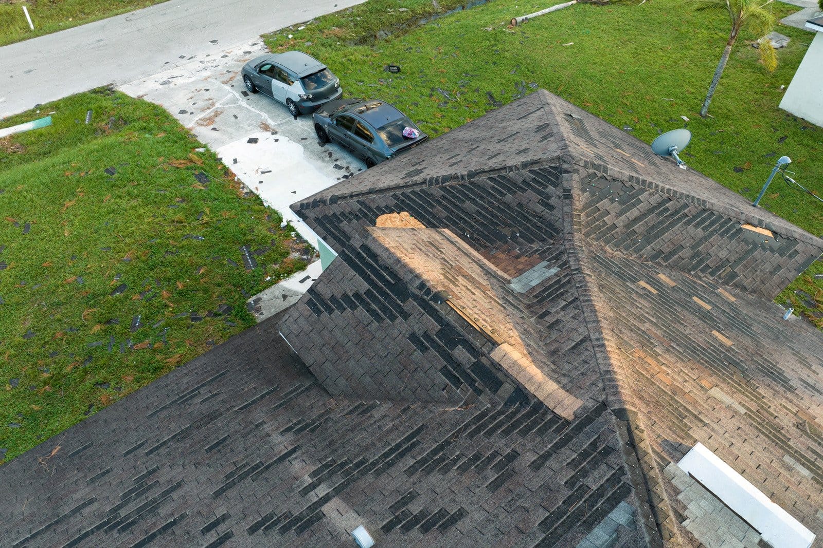Storm-damaged asphalt shingle roof with missing sections and exposed decking after severe wind damage inspection