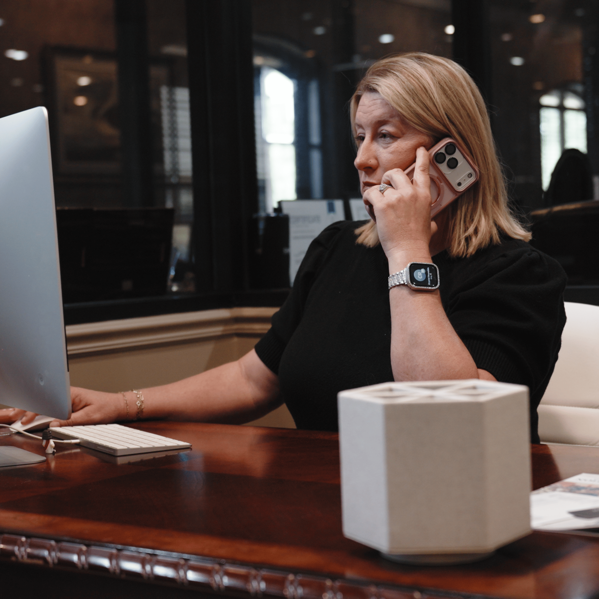 Real estate agent speaking with a client on the phone while working at a desktop computer inside a modern real estate office