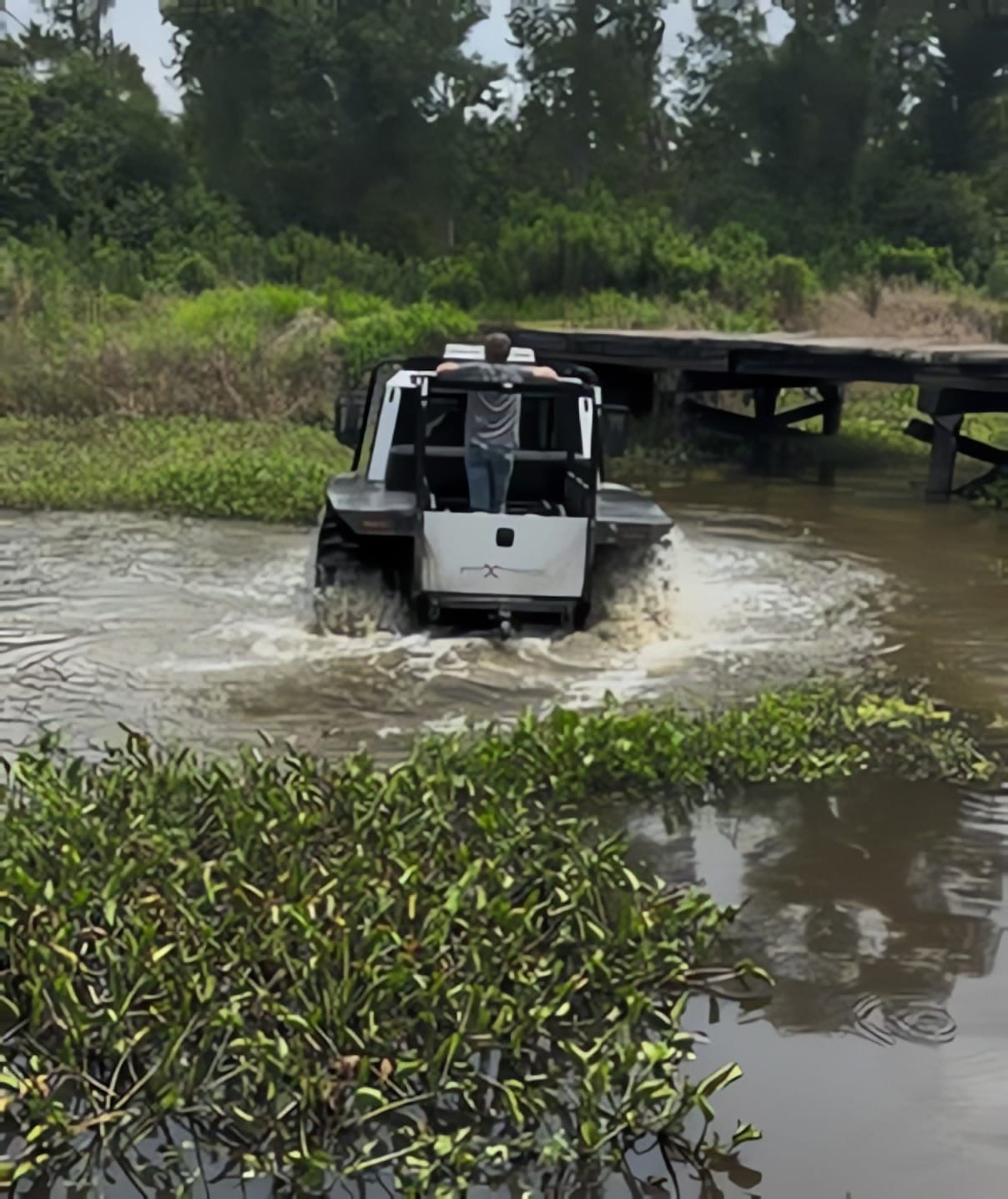 Man standing in the back of a fat truck as it moves through marshy terrain