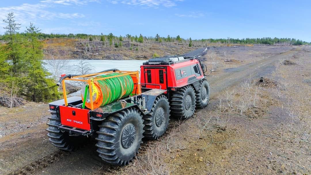 Orange Fat Truck with trailer hauling equipment as it moves along a muddy dirt terrain