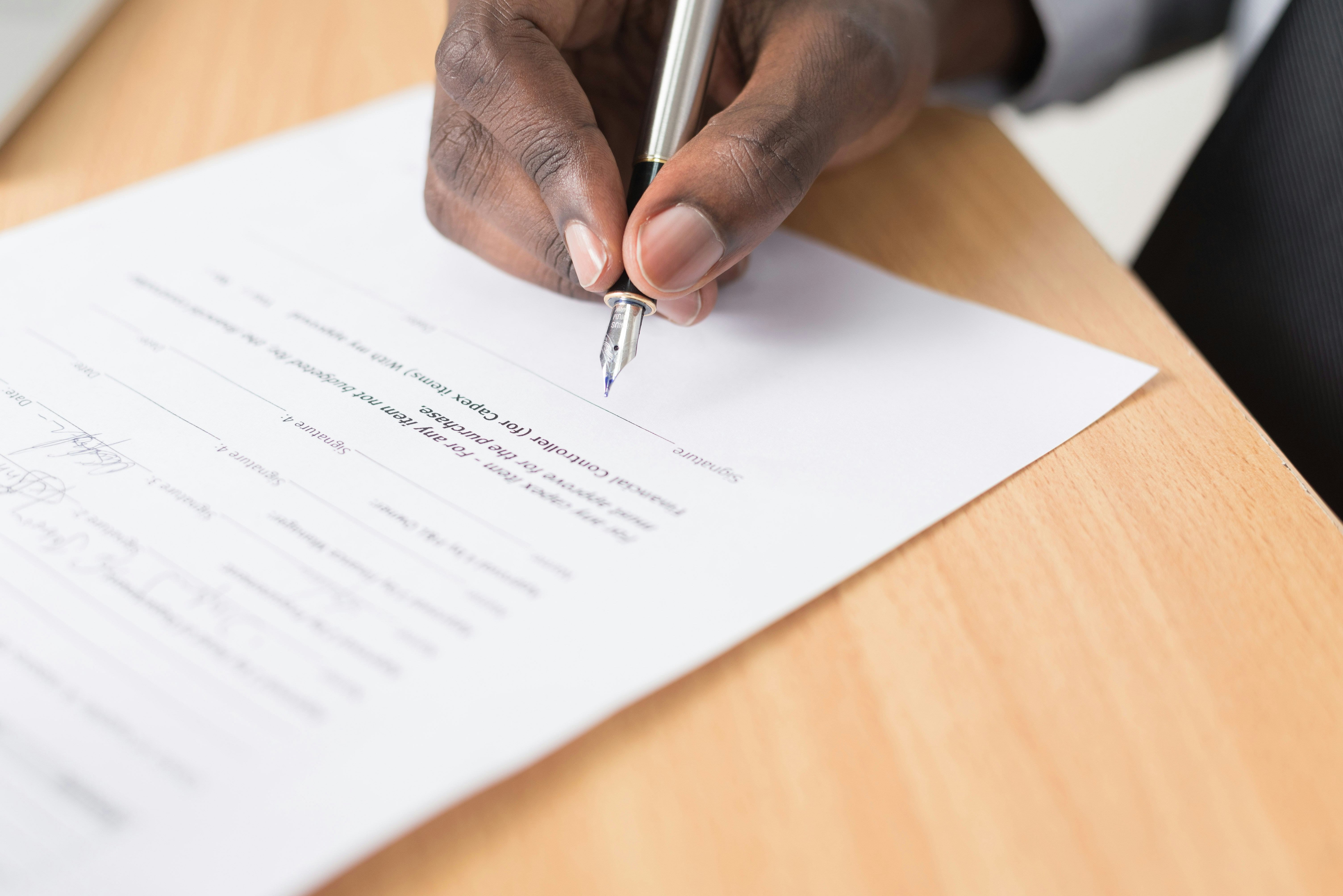 a hand signing documents with a pen