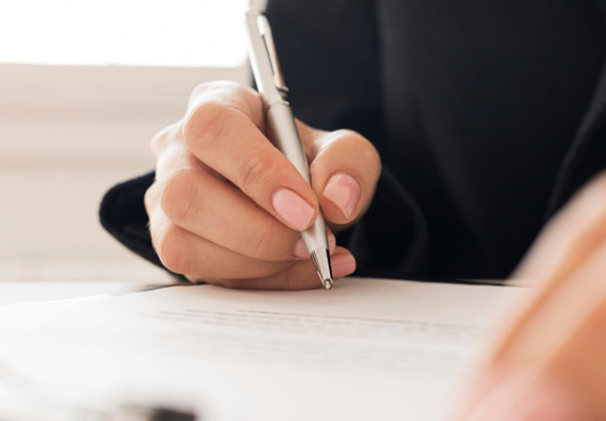 Woman with light pink nails writing with a pen