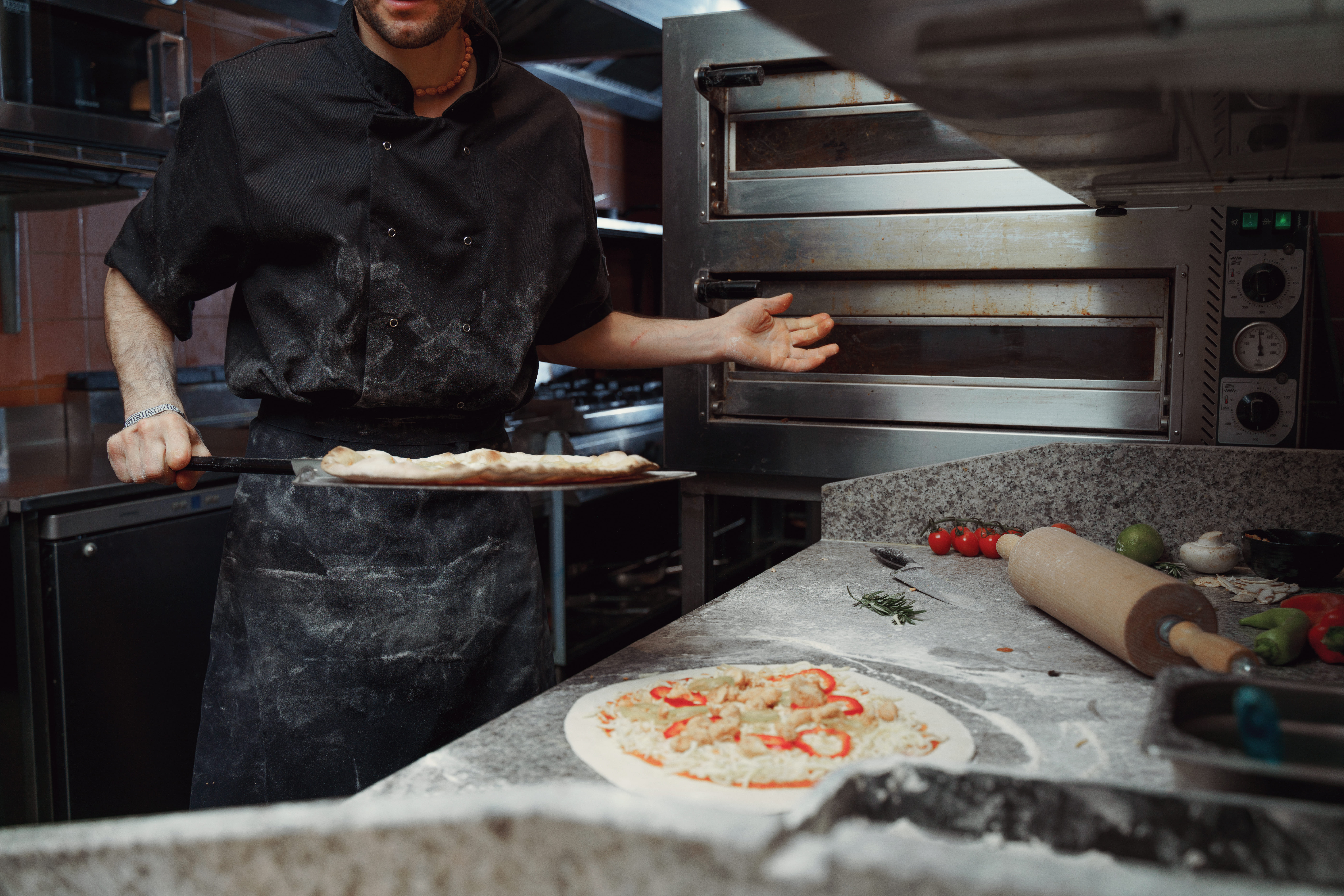 Pizza chef preparing dough next to a commercial deck oven in a restaurant kitchen