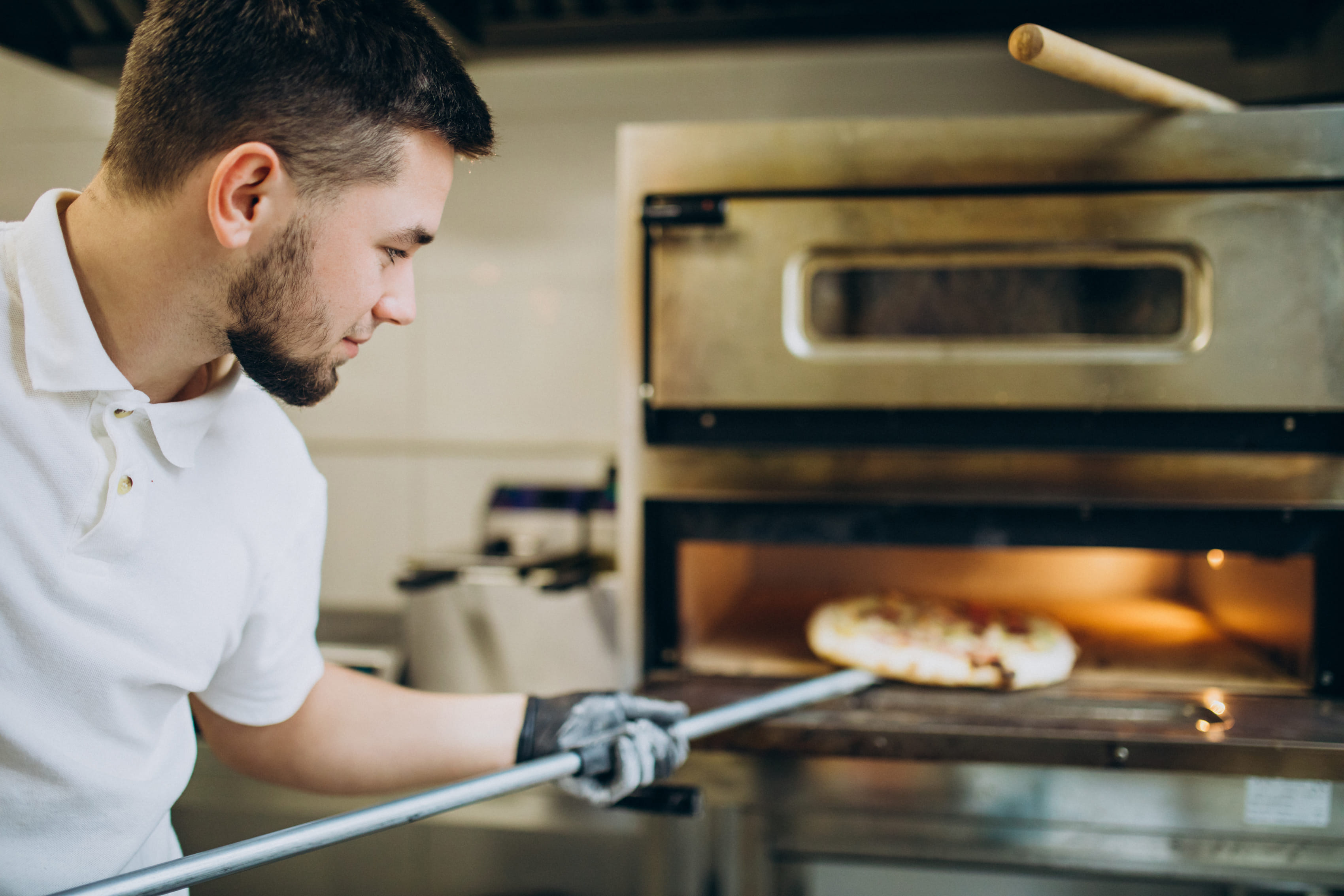 Restaurant worker removing pizza from a commercial oven using a peel