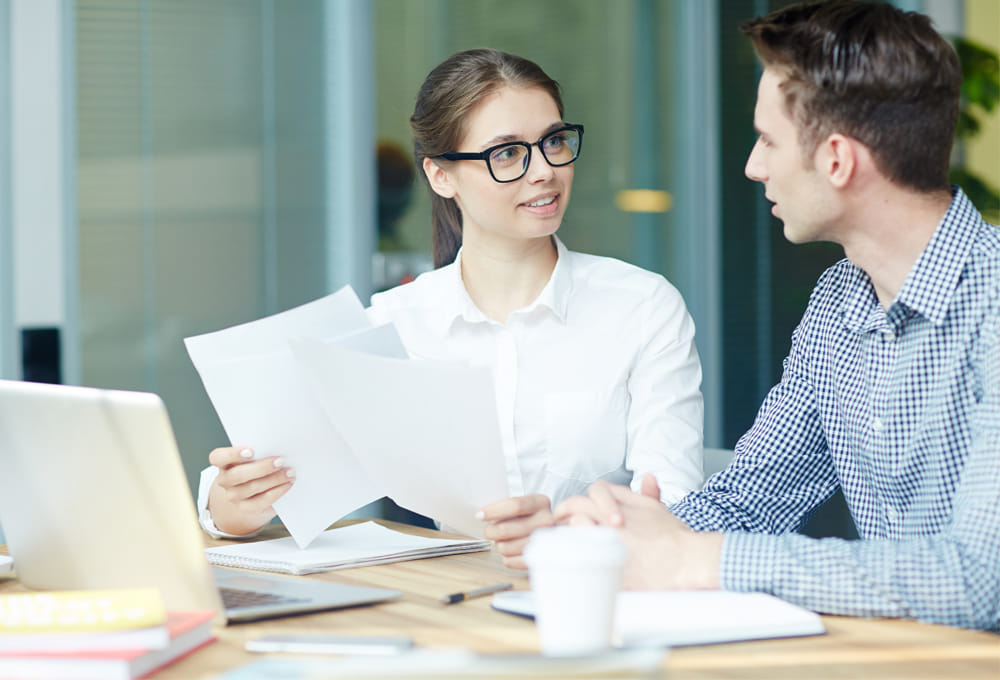 young woman with glasses is talking to a colleague