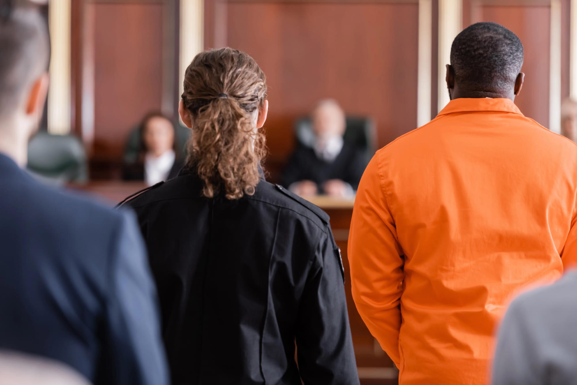 man in orange jumpsuit standing in front of judge in court room