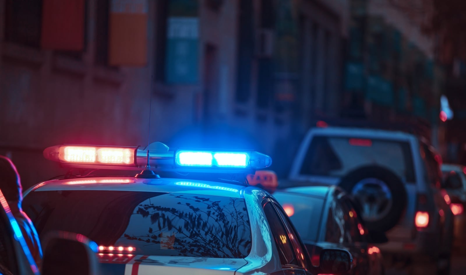 Blue lights on top of the cop car lit up as the car sits behind another vehicle on the road