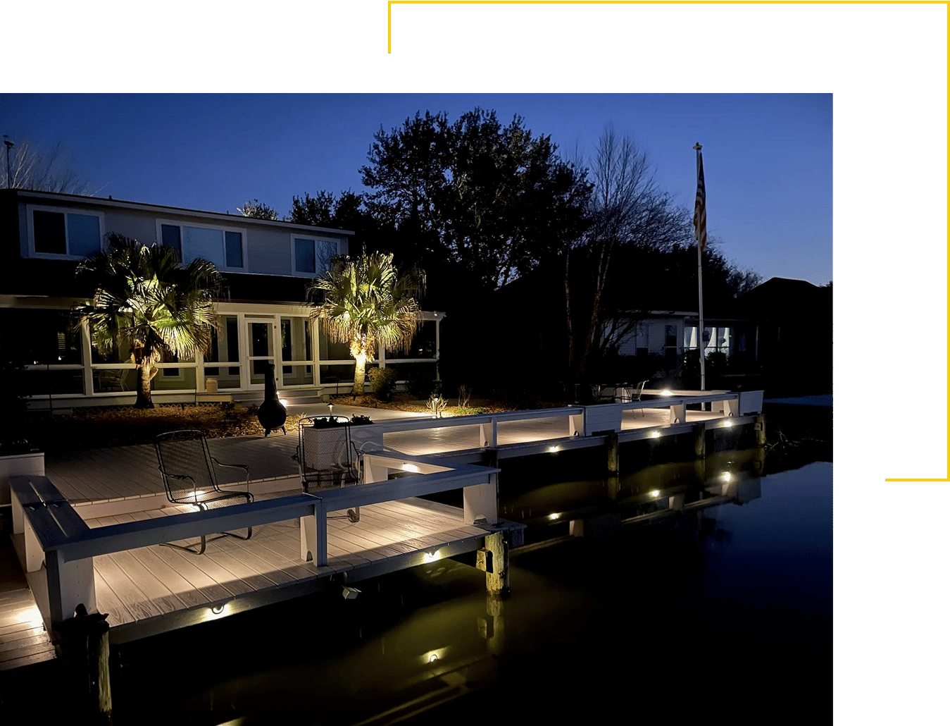 Illuminated dock on a lake behind a residential home at dusk.
