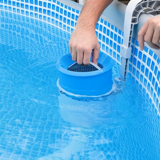hand pulling floating pool chemical dispenser out of pool water