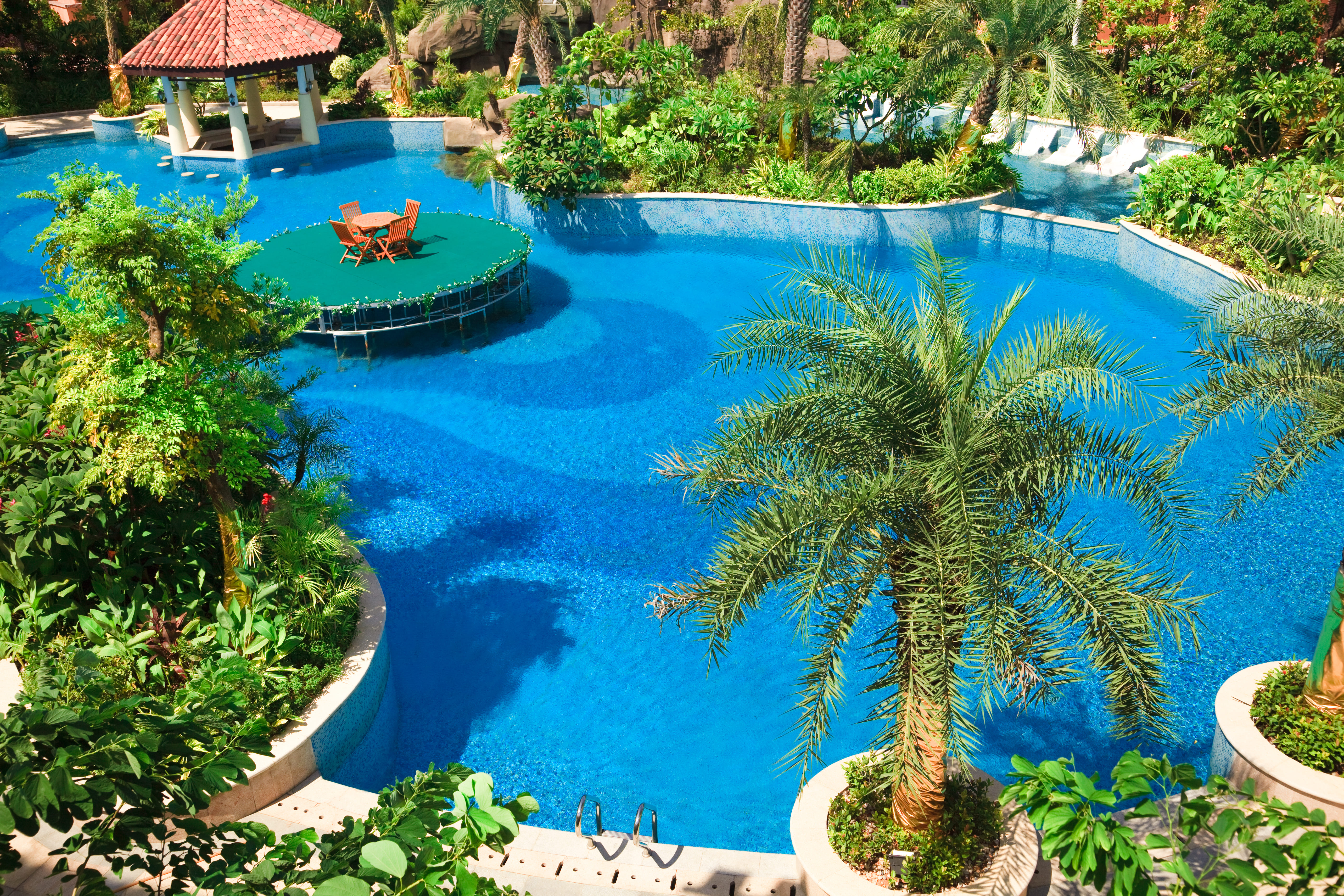 blue water in pool surrounded by tropical trees and a spanish tile gazebo