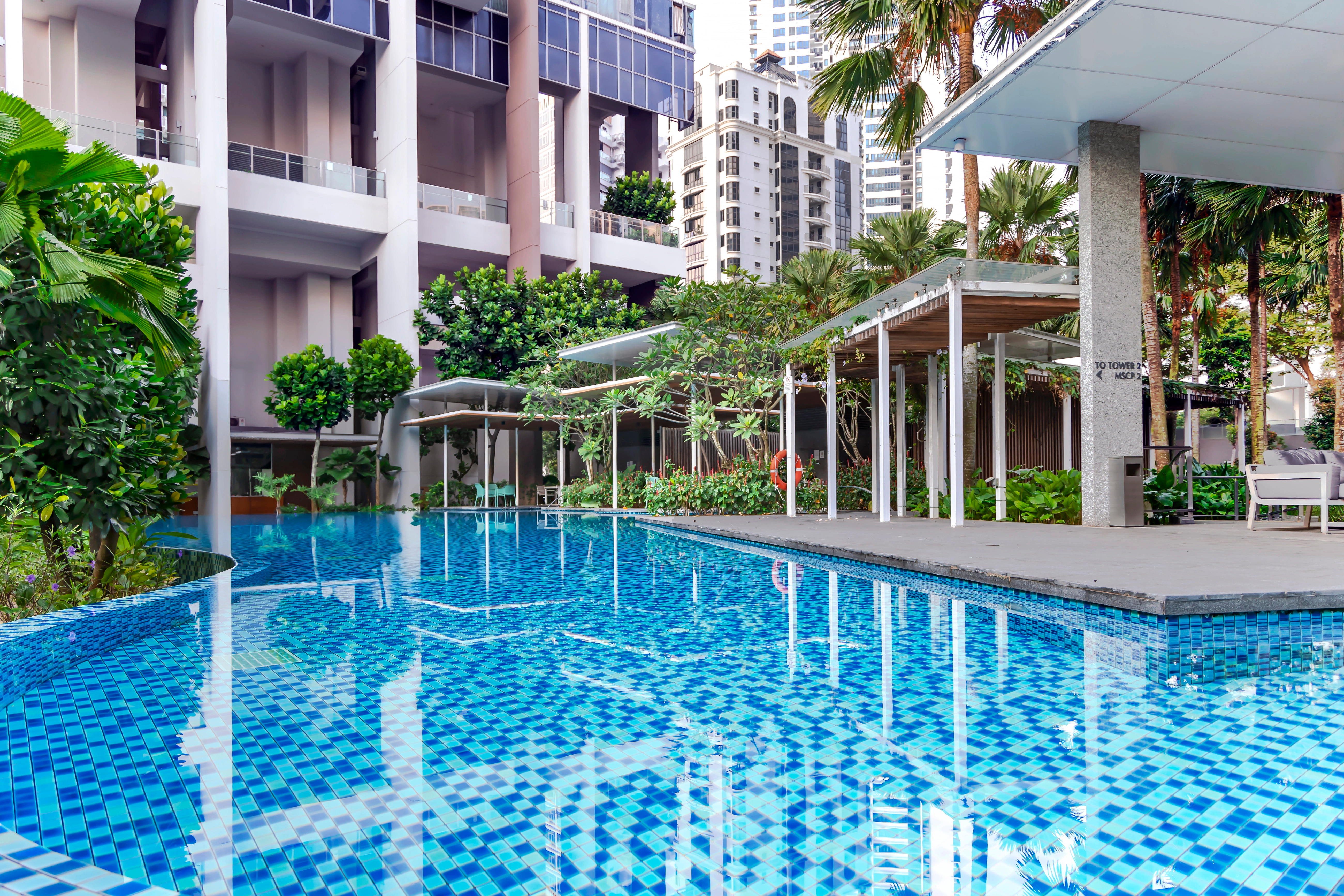 Blue-tiled commercial pool at a high-rise residential complex surrounded by tropical plants and covered seating areas
