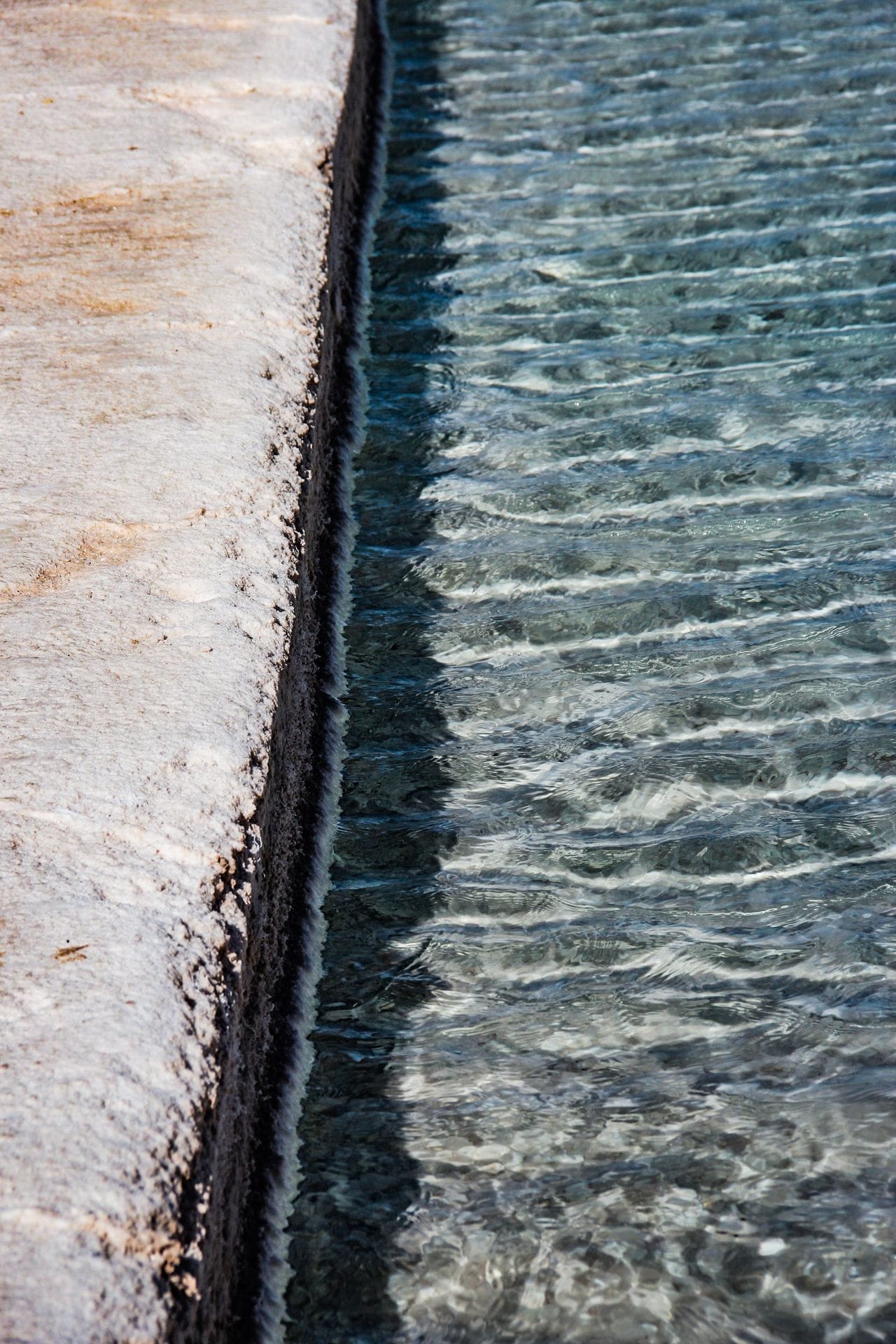 blue water in pool moving against stone wall