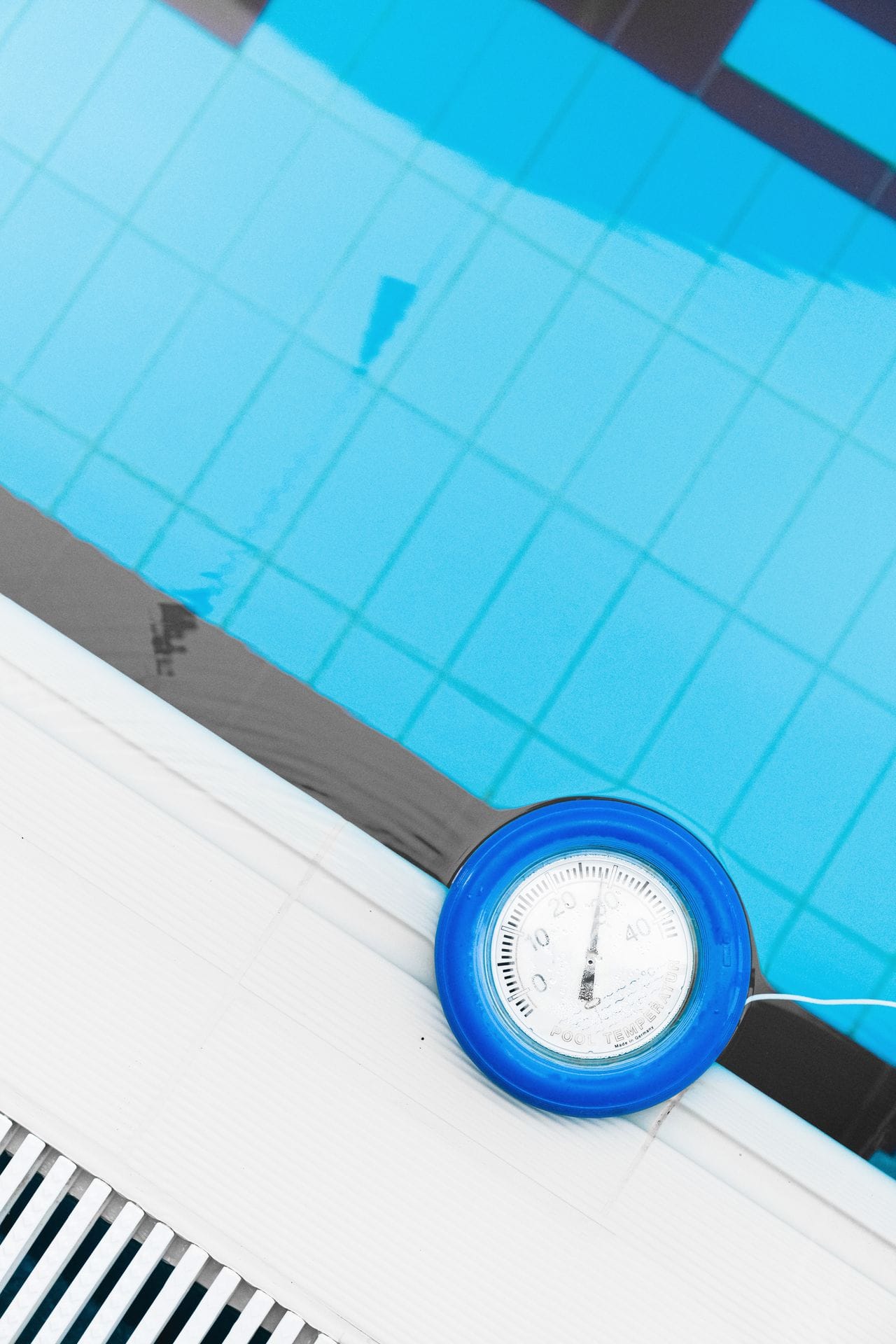 Round pool temperature gauge resting on tiled pool edge