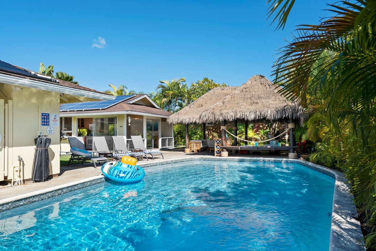 Tropical backyard pool with thatched-roof cabana and lounge chairs