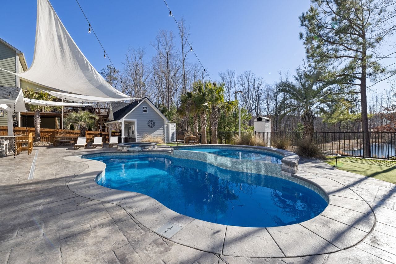 Freeform swimming pool with shade sail and stone patio in backyard