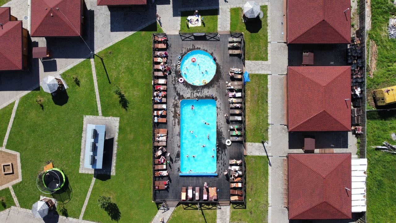 Aerial view of round and rectangular pools at vacation resort with cabins