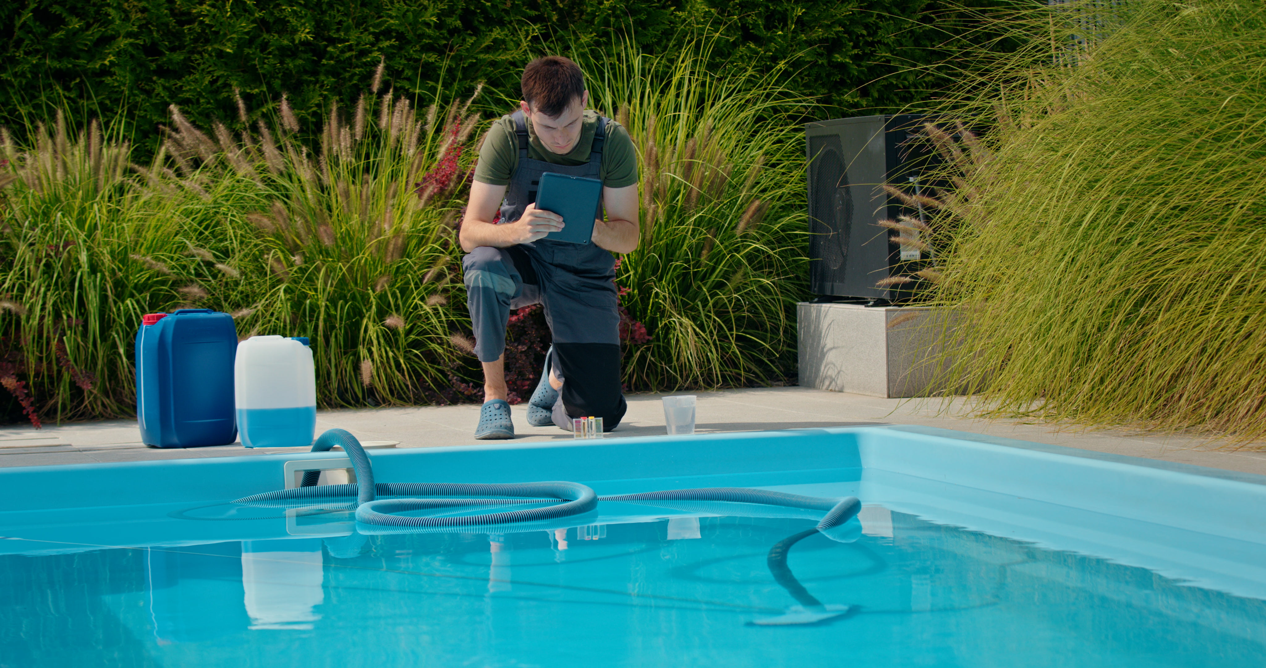 Pool technician checking water conditions with a tablet beside a swimming pool