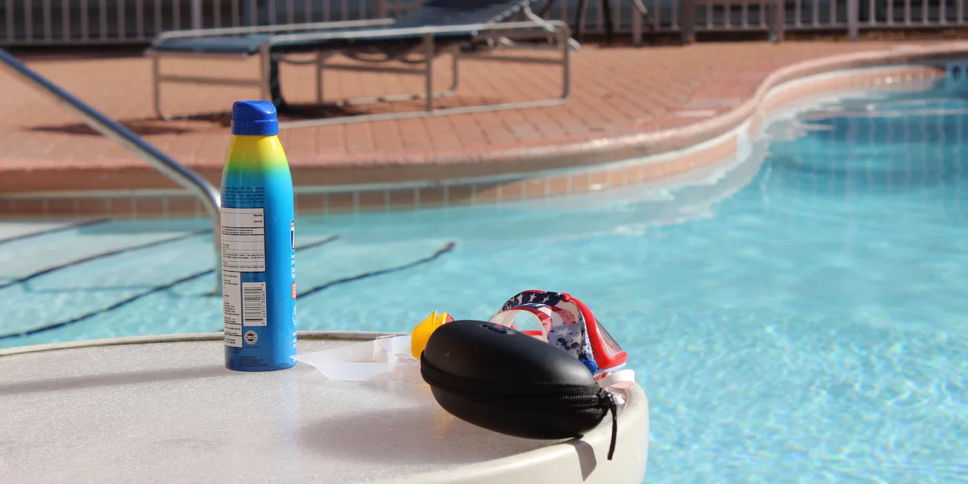 Bottle of sunscreen and swim gear beside a swimming pool