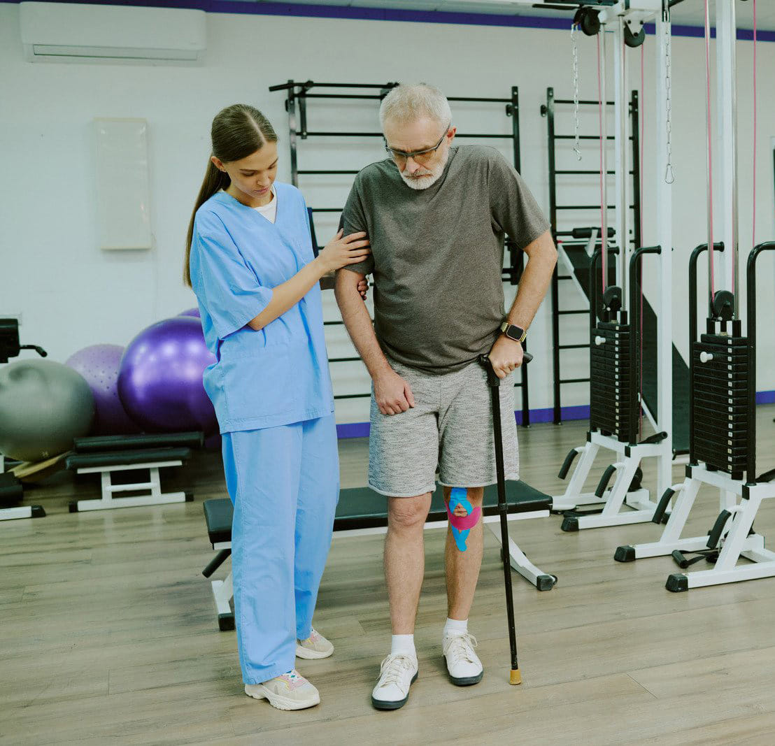 older man with cane getting help from physical therapist