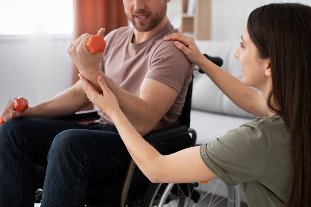 A patient in a wheelchair using hand weights with help of a physical therpaist
