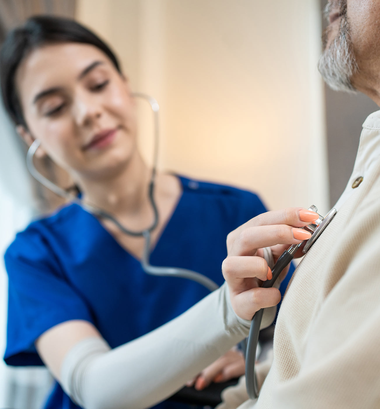 A nurse in blue scrubs calmly checking pateint\'s heart rate in an office