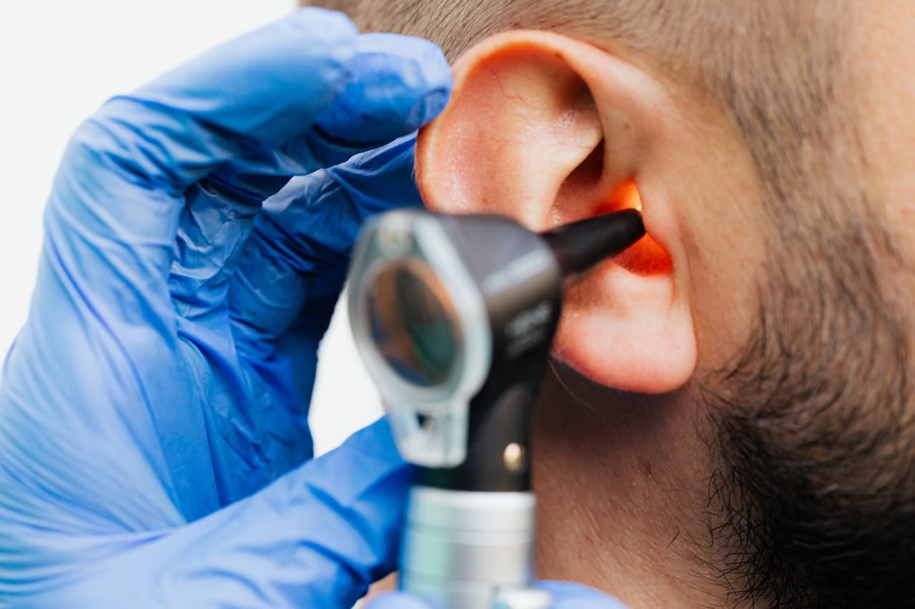 ENT specialist examining adult patient’s ear with otoscope during in-office diagnostic exam
