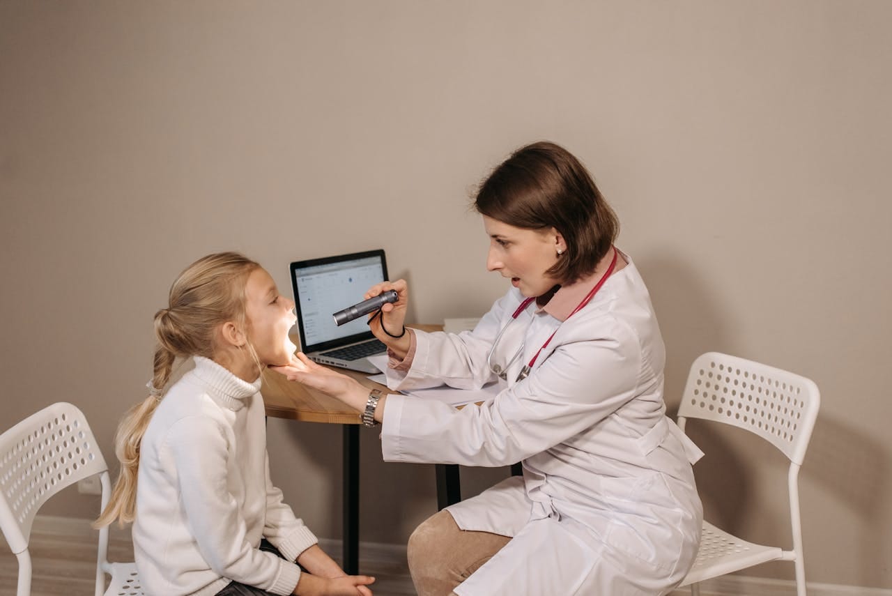 Pediatric ENT doctor examining young child’s throat during office visit
