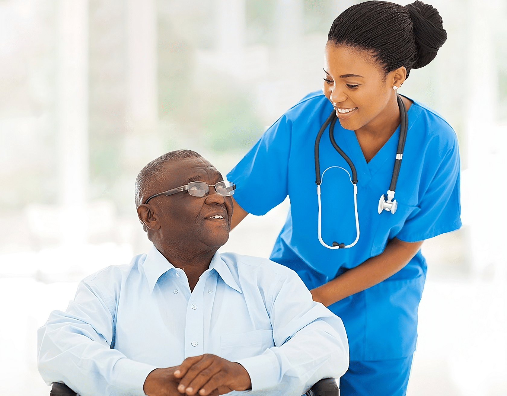 A healthcare worker assists an elderly patient in a wheelchair with a caring smile.