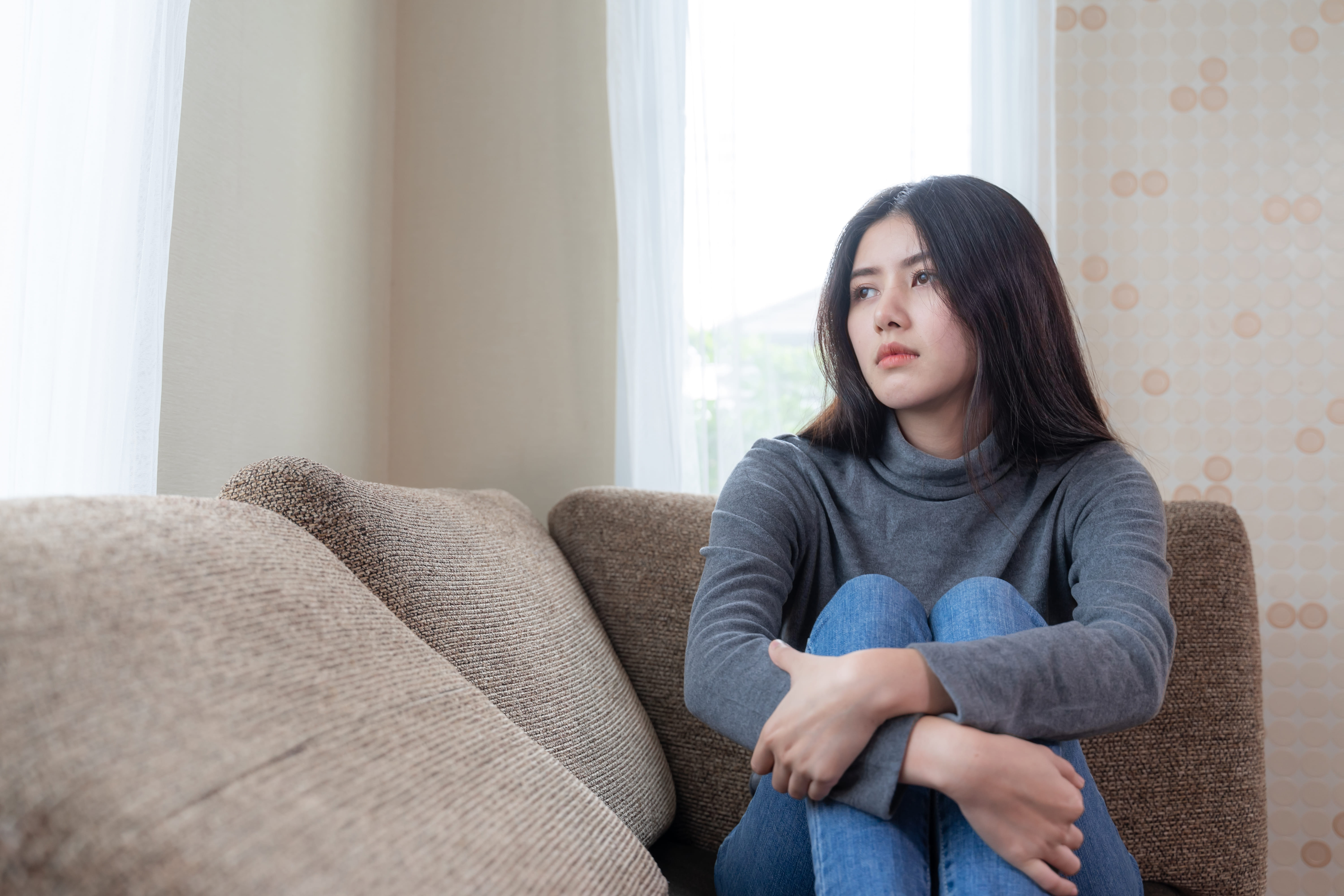 tired young woman sitting alone on couch with feeling sad