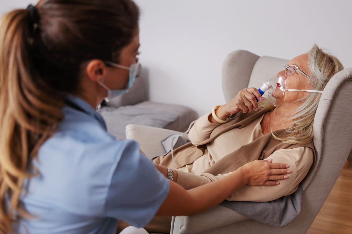 patient holding breathing mask to her face as she sits in chair