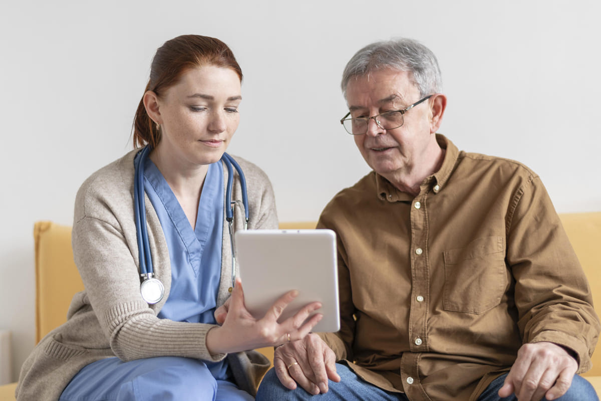 Hospice care physica holding Ipad speaking with elderly man