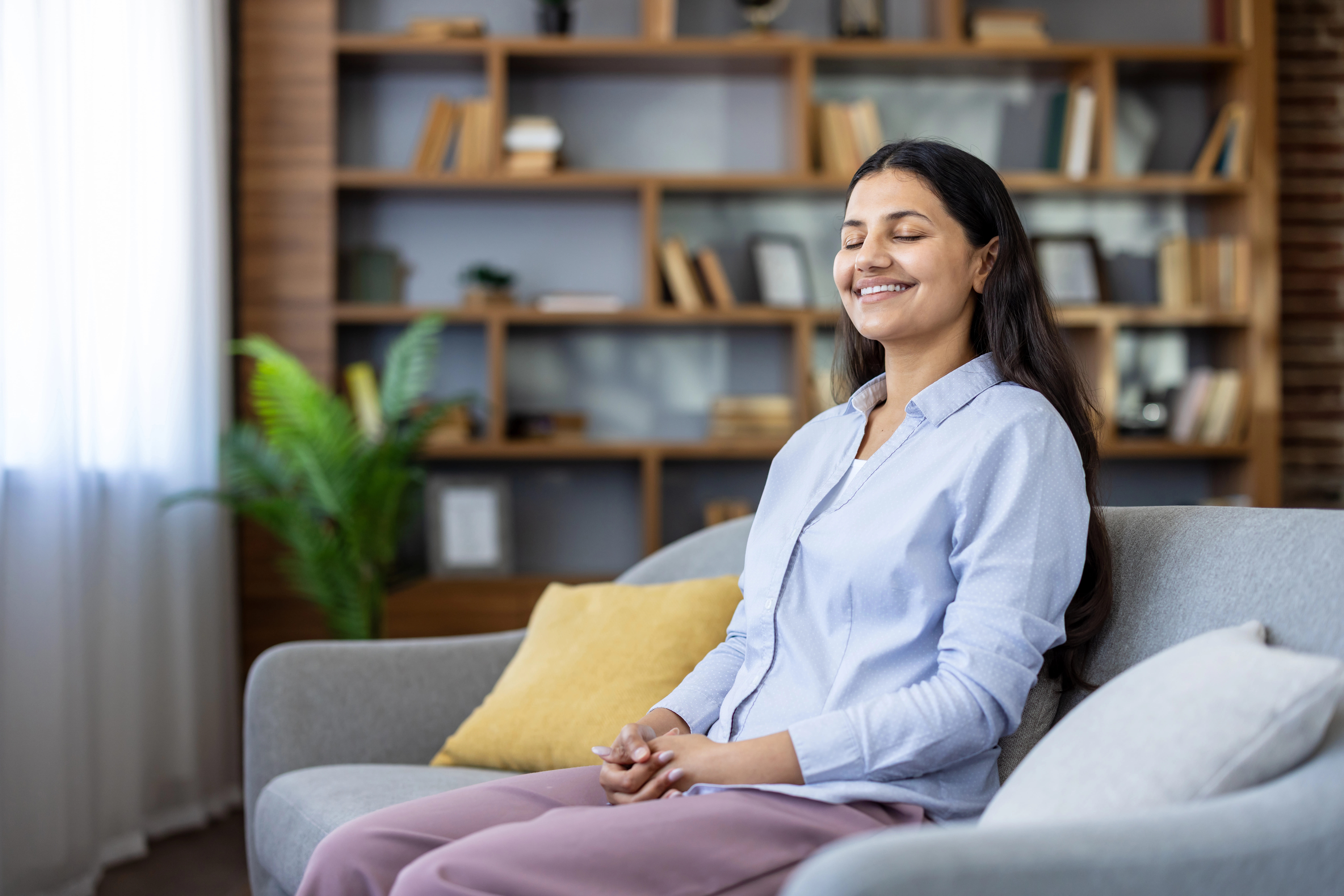a woman smiling with her eyes closed as she sits on a couch