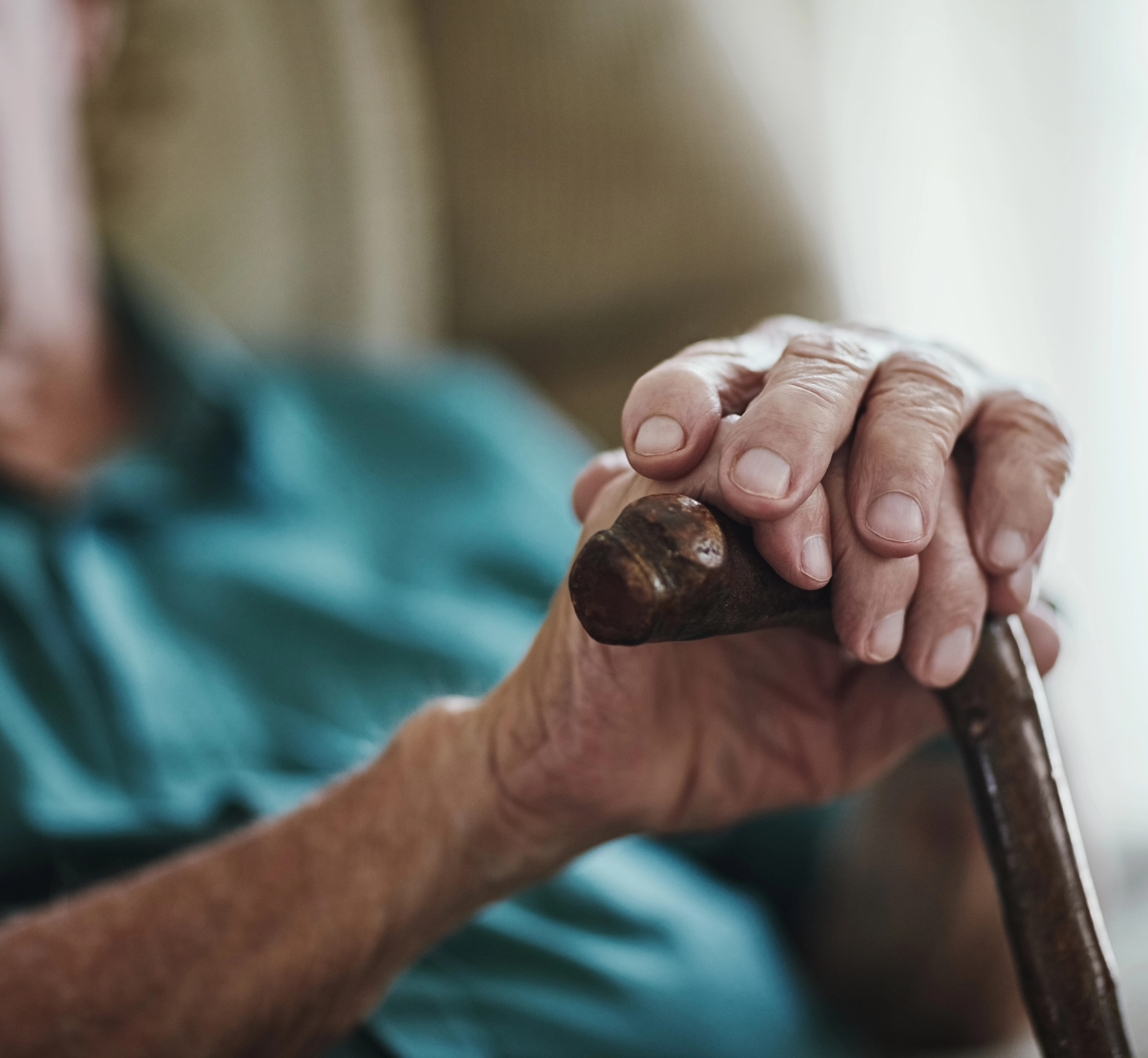 elderly hands folding over the handle of a cane