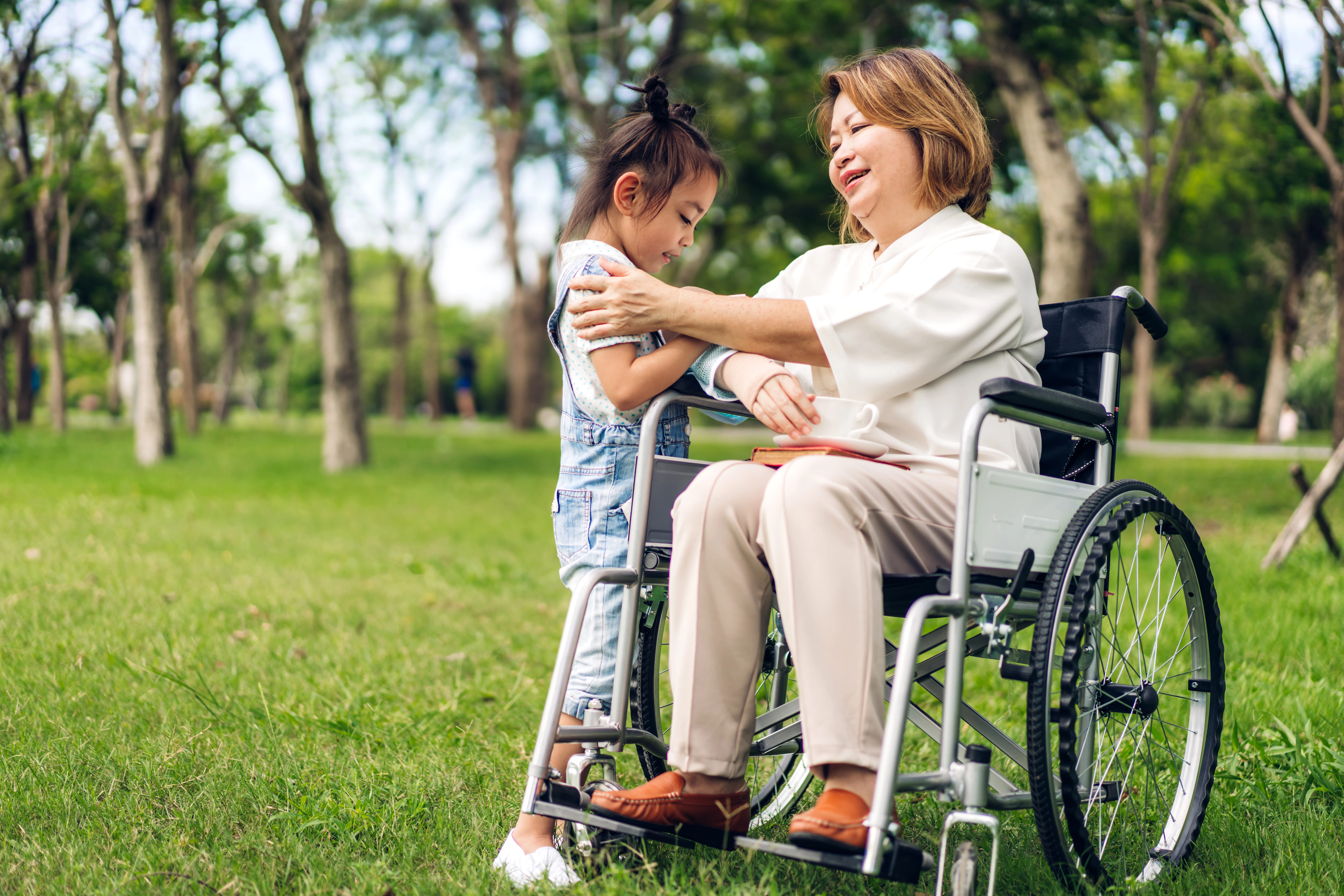 Woman sitting in wheelchair with a cup of tea spending time with granddaughter