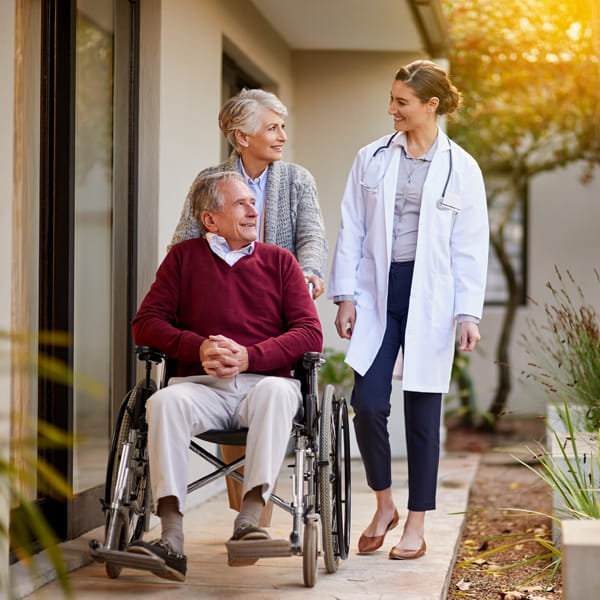 Elderly man being pushed in wheelchair by his whife as they speak with doctor