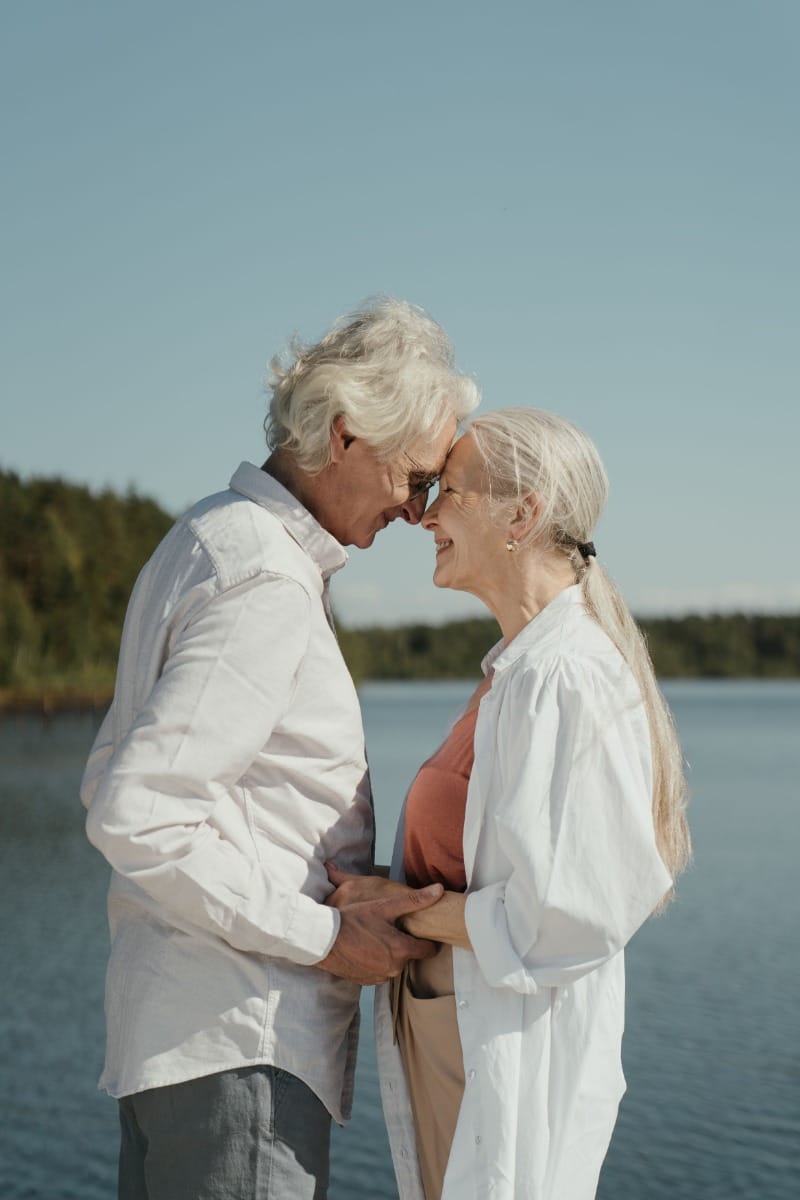 Elderly couple holding hands and leaning into eachother near a scenic lake