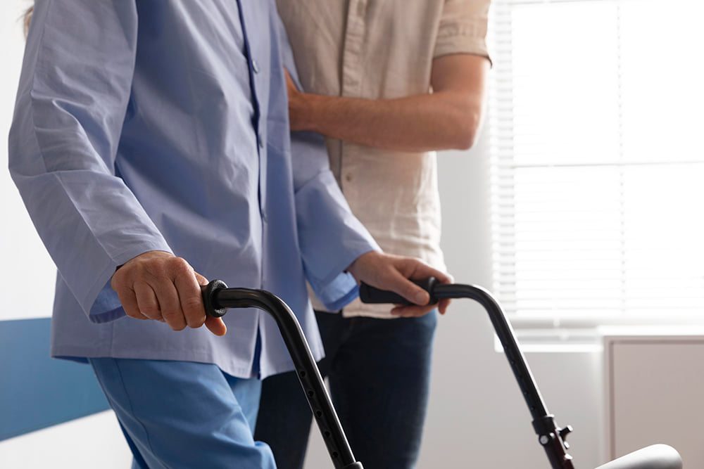Elderly man holding walker as he walks with assistance