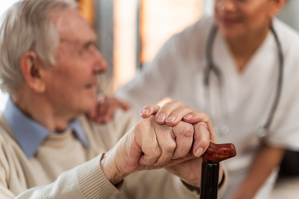 Elderly man holding onto his wooden cane as he speaks to a doctor
