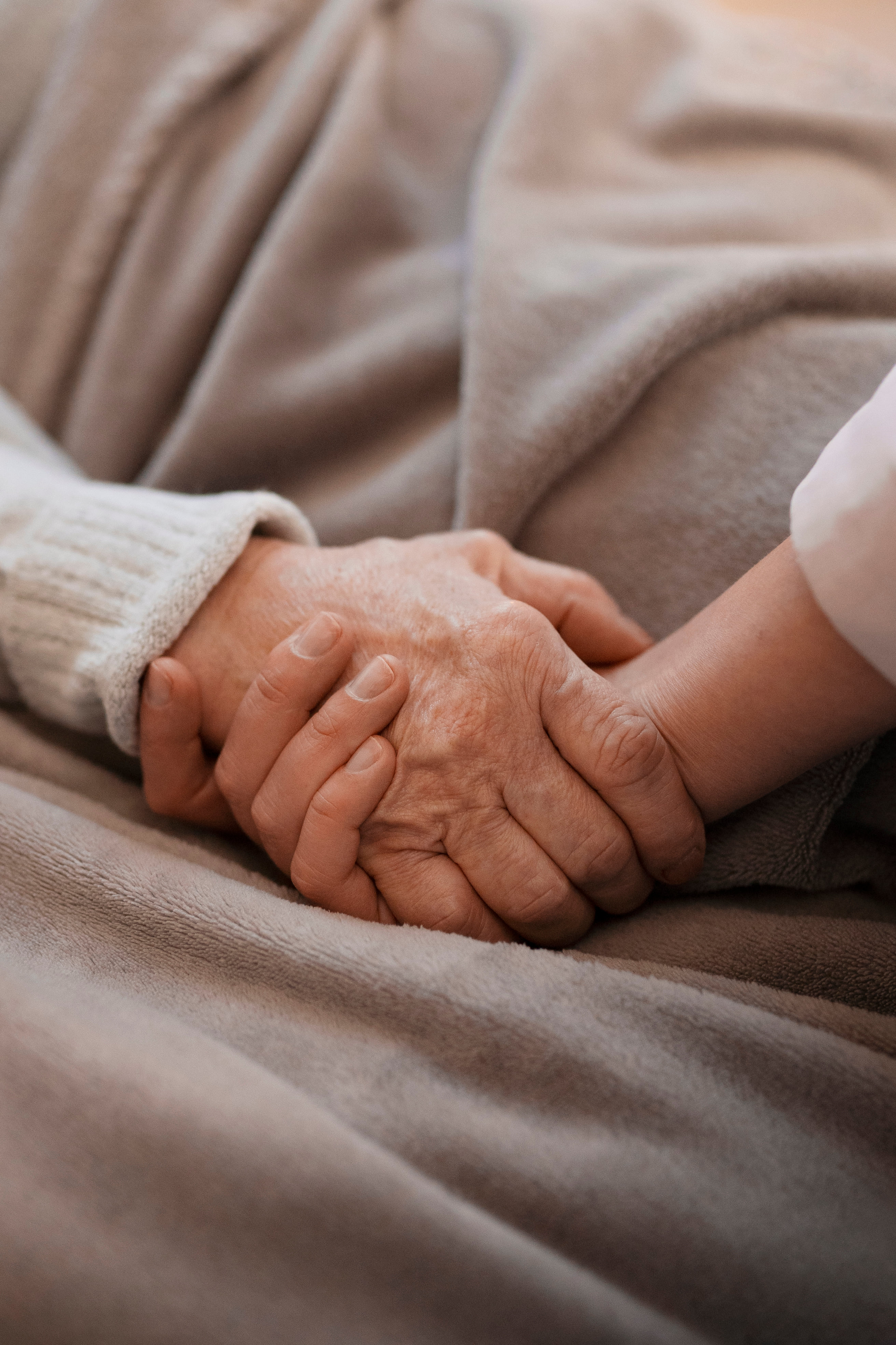 Close-up of a caregiver gently holding an elderly woman\'s hand to provide comfort and reassurance