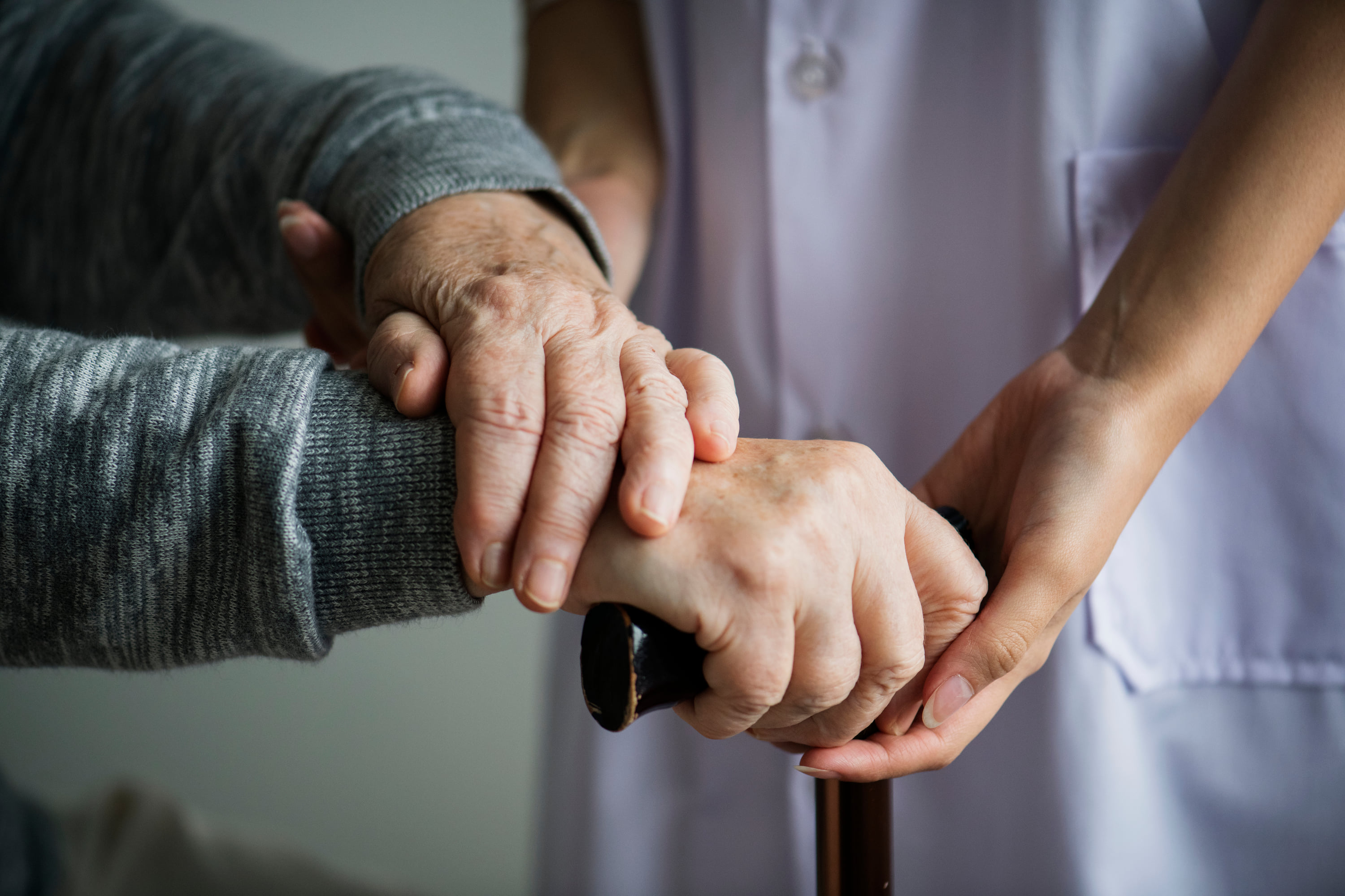 Caregiver gently supporting an elderly patient\'s hands while assisting with a walking cane