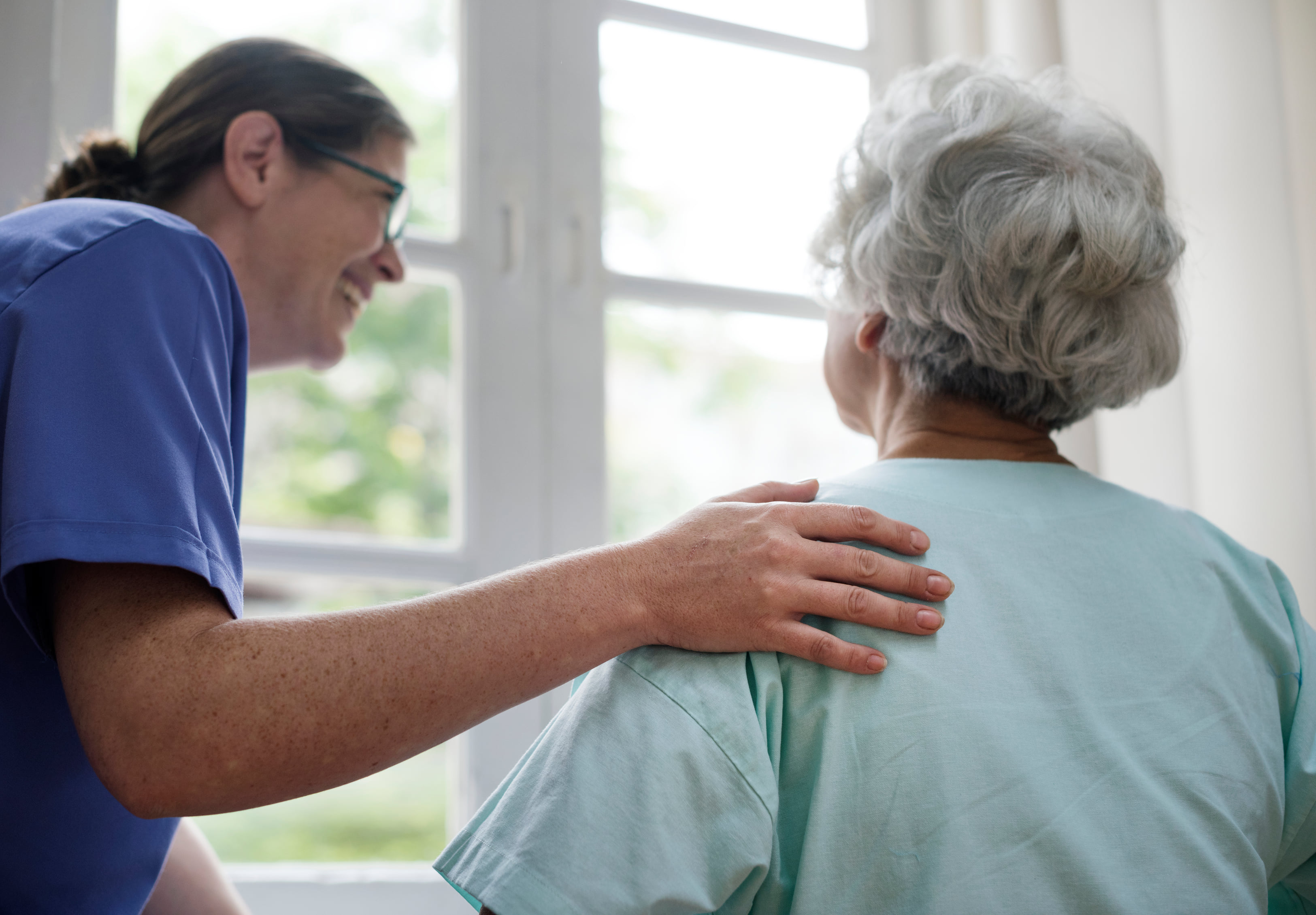 Nurse offering comfort to an elderly woman by placing a reassuring hand on her shoulder