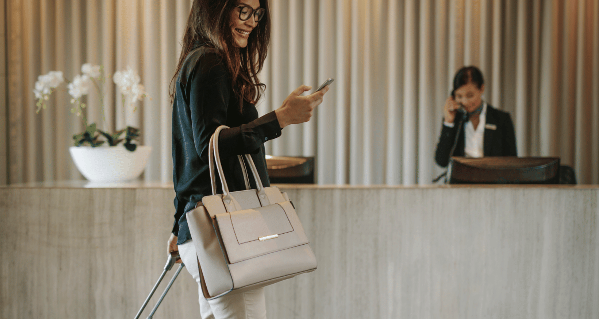 Woman checking her phone while walking through hotel lobby with luggage