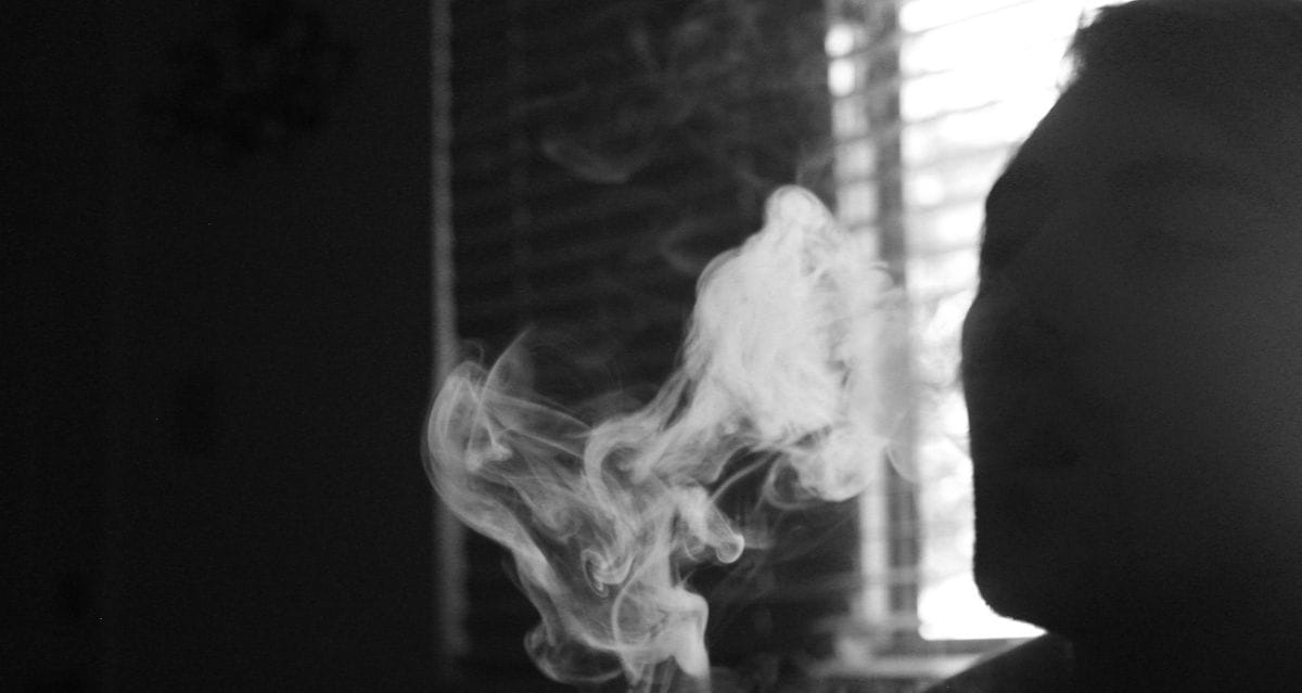 Silhouette of person exhaling vape smoke near window