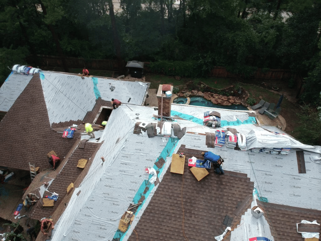 Roofer laying new shingles over synthetic underlayment during a roof replacement on a Katy home, with shingle bundles staged across the deck