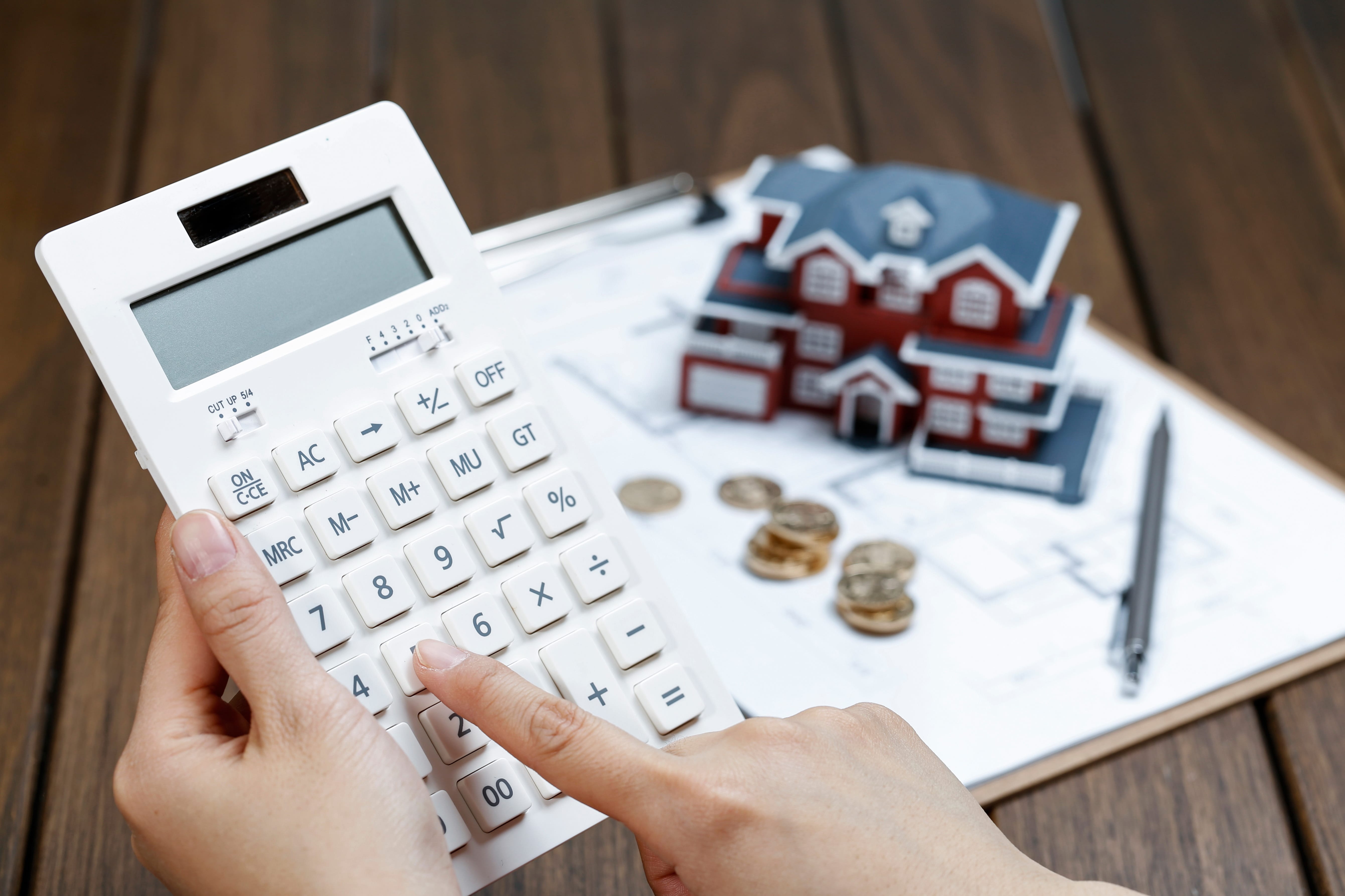 Calculator and coins next to a model home and paperwork, illustrating FHA closing costs, loan calculations, and cash-to-close planning.