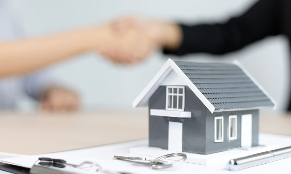 Model home with keys and handshake in the background.