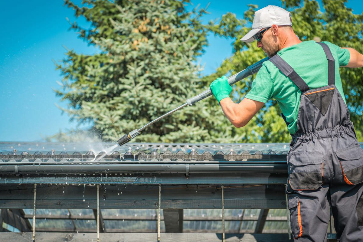 Technician cleaning roof surface with pressure washer during roof maintenance